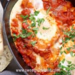 Closeup overhead view of shakshuka in a grey oval skillet with crusty bread on the side