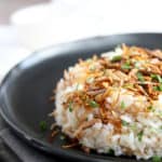 Close-up angled side view of simple Arabic white rice with vermicelli on a black dish topped with toasted nuts and parsley