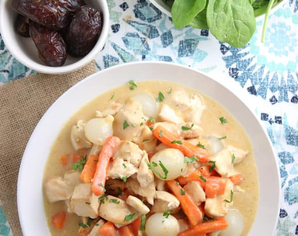 overhead of white bowl with chicken , carrots, potatoes in a cream based sauce on a moroccan pattern placemat