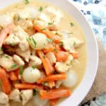 close up overhead of white bowl with chicken , carrots, potatoes in a cream based sauce on a moroccan pattern placemat