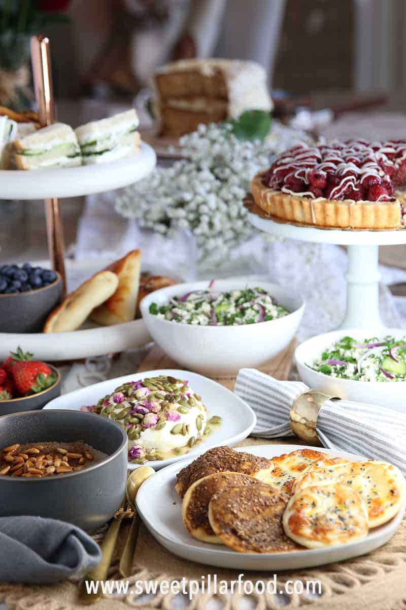 Side view of several white plating with bread, salads, cheese dome, tart and sanwiches