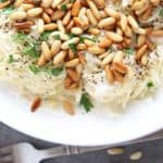 overhead of white plate with thin spaghetti topped with toasted pine nuts and parsley garnish