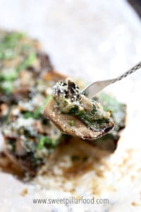 close up of a slice of spinach stuffed portable mushroom on a fork with remaining portebello mushroom blurred out in the background