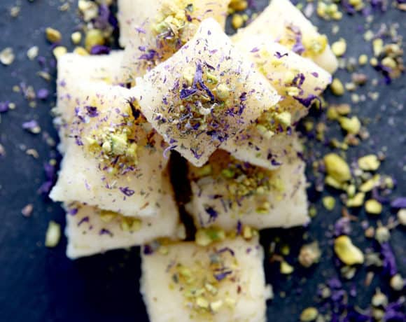 Overhead shot of a pile of sweet cheese rolls on a slate board with pistachios and lavender sprinkled on top